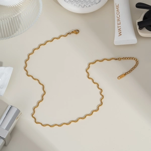 Close-up of golden wavy snake chain necklace with lobster clasp on beige surface