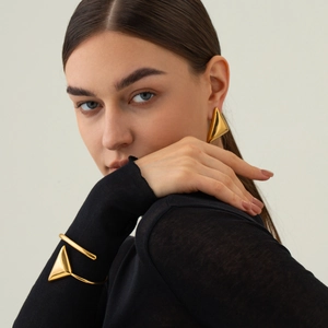 Close-up of golden geometric triangle earrings and matching bangle worn by a model