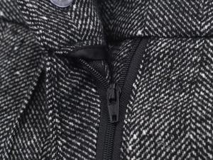 Macro shot of black and white herringbone tweed fabric with zipper closure and button detail