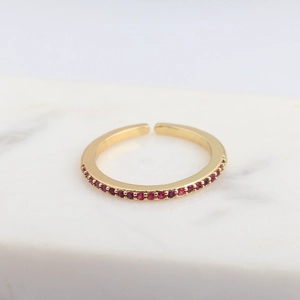 Macro shot of an adjustable gold ring featuring small red cubic zirconia stones on marble