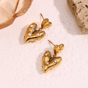 Macro shot of 18K gold heart earrings with white pearls on a wet water-drop background