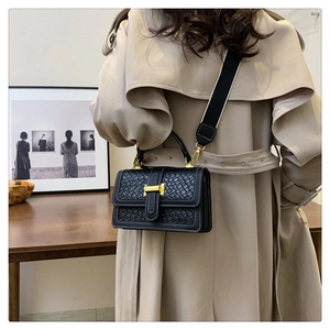 Detail view of woven black crossbody bag with gold lock on a beige trench coat