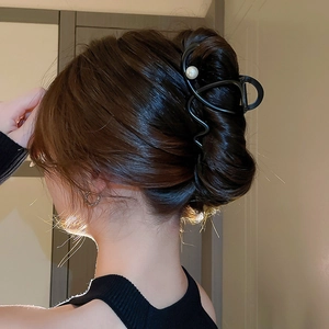Rear view of a large black metal wave hair claw clip with a pearl on dark brown hair
