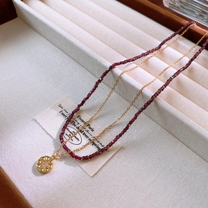Close-up of double-layer necklace with gold sunburst pendant and deep red beads on velvet tray