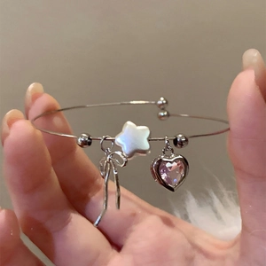 Close-up of silver open bangle featuring bow, pink heart crystal, and star charms