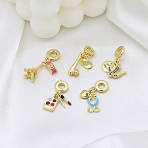 Golden charms set with Eiffel Tower, perfume bottle, and lipstick on white silk background
