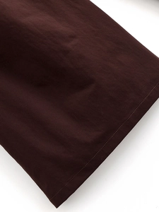 Dettaglio della trama del tessuto marrone scuro e cuciture precise sui pantaloni larghi