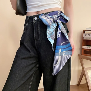 Dettaglio di un foulard in raso blu navy usato come cintura su jeans in denim scuro