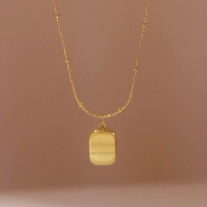 Polished gold rectangular pendant necklace with bead chain on beige background