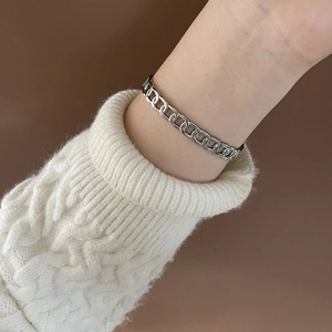 Close-up of a silver-toned chain link bracelet on a wrist with a white knitted sweater