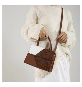 Detail of a brown crocodile pattern and white leather shoulder bag held by a model