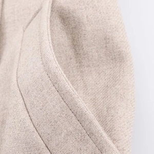 Dettaglio cuciture ad alta densità sul bordo della tasca di un cappotto di lana beige