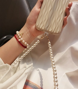 Detail of white pearl crossbody phone strap attached to a beige textured case
