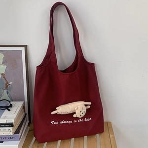 Detail of burgundy canvas tote bag with plush kitten pendant and shoulder strap