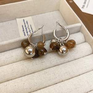 Detail of silver drop earrings with brown resin beads on a beige velvet jewelry box