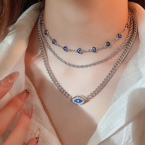 Close-up of layered silver necklaces with blue evil eye pendants on a white shirt