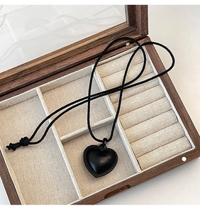 Gros plan d'un collier cœur noir avec cordon tressé dans un écrin à bijoux en bois