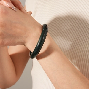 Detailed view of deep green polished jade bangle worn on wrist with soft lighting