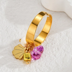 Gold titanium open ring with purple stone and shell charms on light textured background