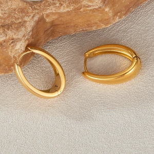 Close-up of golden oval water-drop earrings with polished finish on white textured stone