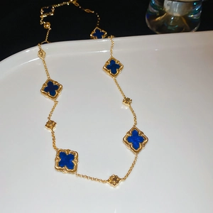 Macro detail of gold plated necklace with blue clover motifs and intricate bead edging