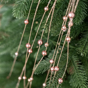 Rose gold Christmas bead garland hanging on green pine branches for festive tree decoration