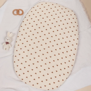 Macro shot of oval baby cradle fitted sheet in beige cotton with brown heart print