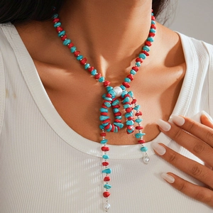 Detail of beaded necklace with turquoise and coral stones and pearls on a white top