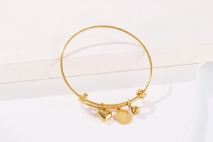 Detail of gold-plated bangle with queen coin, heart charm and steel bead accents