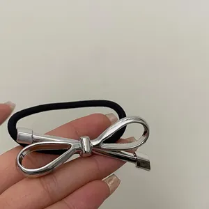 Detail of a large silver hollow bow ornament on a black elastic ponytail hair tie