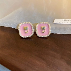 Close-up of pink square earrings with golden tulip motif and pearl border on wood