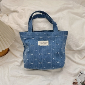 Détail du sac cabas en jean avec imprimés nœuds et cœurs blancs sur une surface en tissu