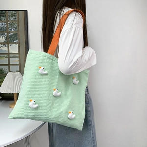 Detail of green striped canvas tote bag featuring cute 3D duck dolls and orange handles