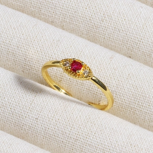 Close-up of gold ring with oval red gemstone and clear cubic zirconia on beige fabric