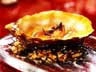 Close-up of golden brown pastry on glass plate with sauce and crushed nut details