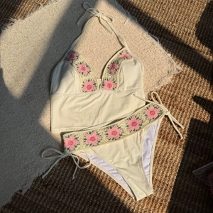 Detail of cream bikini set with pink handmade crochet flower edges on straw mat