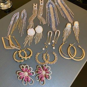 Flat lay of multiple emerald leaf tassel earrings with rhinestones and crystals on grey surface