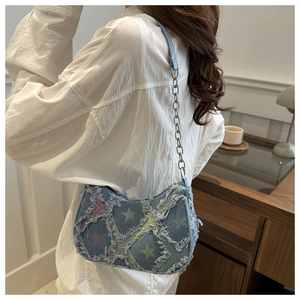 Detail of blue denim shoulder bag with star prints and frayed edges worn by a model
