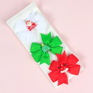 Close-up of three Christmas bow hair clips with Santa and tree motifs on a ceramic tray