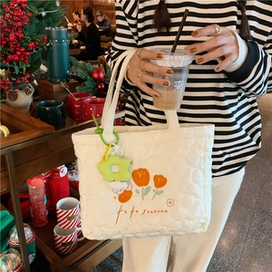 Detail of off-white quilted tote bag with orange tulip embroidery and flower charm