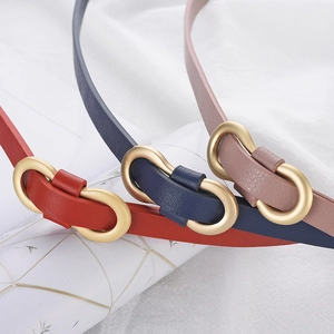Detail of red, dark blue, and pink skinny belts with golden oval buckles on white fabric