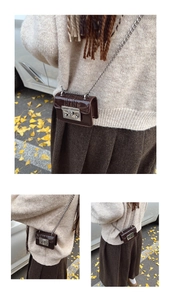 Detail of a dark brown mini patent leather chain bag with silver buckle and mirror finish