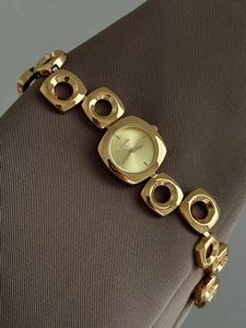 Close-up of a gold irregular hollow link bracelet watch with a square chamfered dial