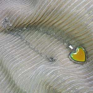 Macro detail of silver heart locket pendant with color-changing glitter on wavy fabric