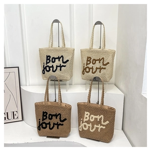 Detail view of woven straw tote bags in four colors with Bon jour embroidery