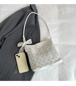 Detailed view of white polka dot bucket bag with lace bow and smartphone for size scale