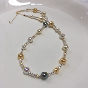 Detail of colorful akoya-style pearls with gold adjustable chain on white ceramic plate
