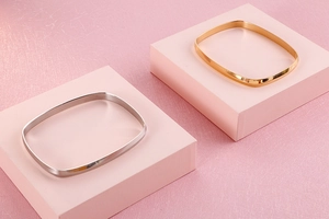 Detail of square gold and silver titanium steel bangles on minimalist pink stands