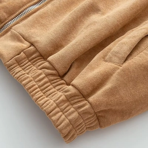 Detail of tan faux suede bomber jacket showing metal zipper and elastic hem texture