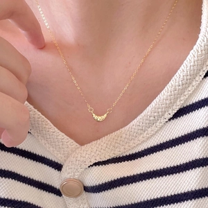 Close-up of a minimalist gold croissant necklace worn by a model for a modern look
